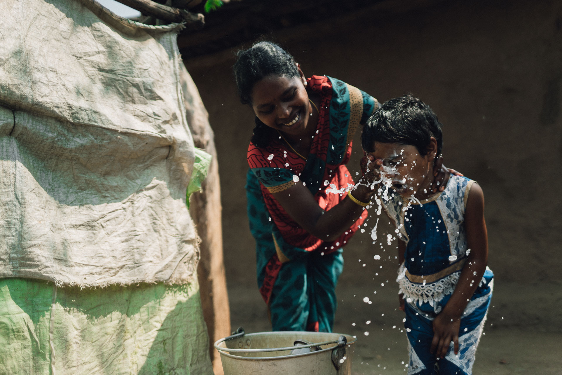 Indian Woman washing her daughter's face at outside pump