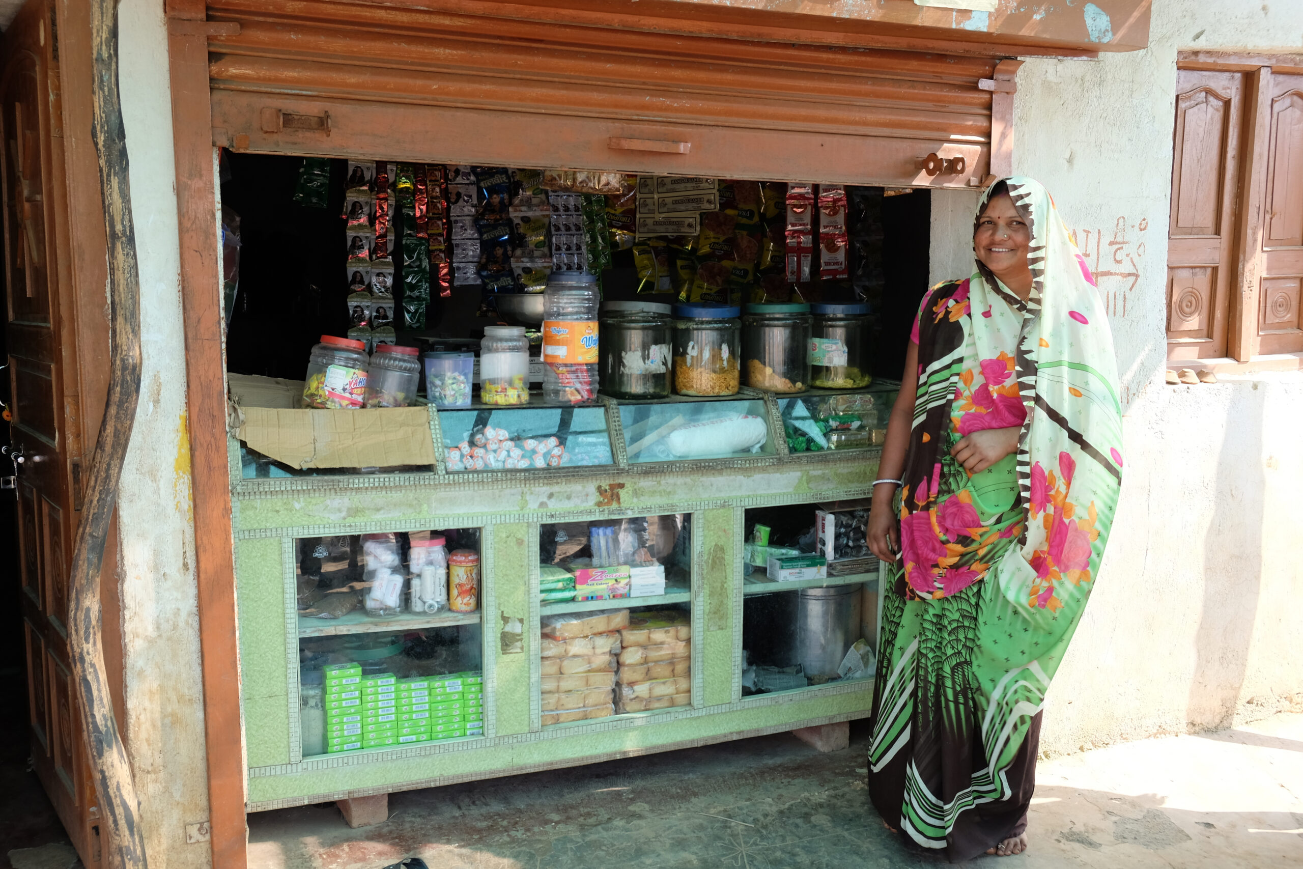 Indian woman stands next to small shop selling tins and packets of food