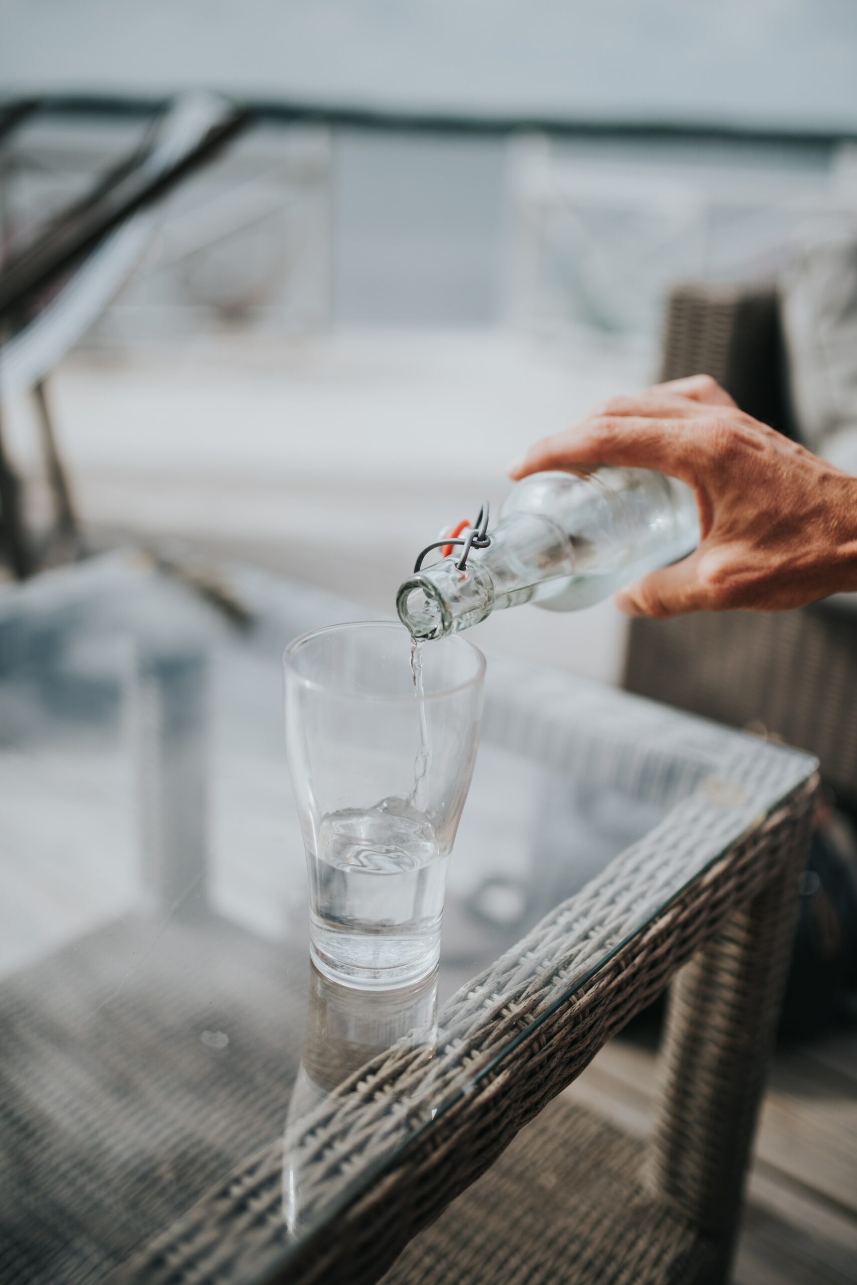 Person pouring tap water from glass bottle into glass on table